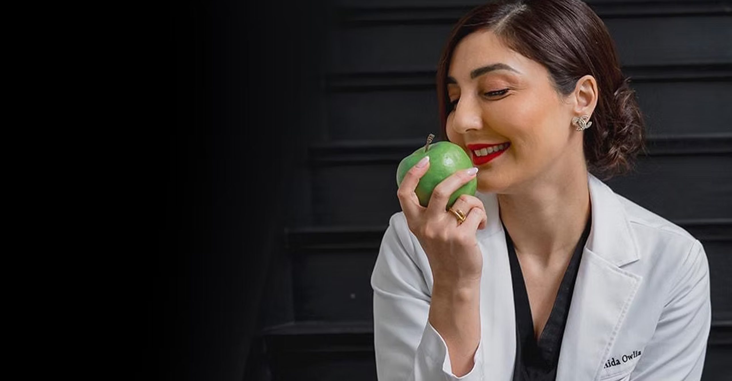 Dr. Owlia Aesthetics physician in a white coat holding a green apple
